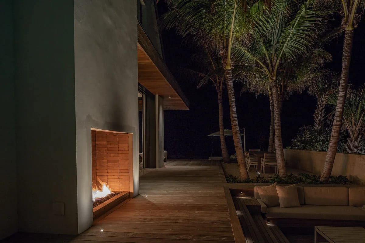 Patio with brick fireplace, wooden decking, beige sofa, palm trees, and additional seating.