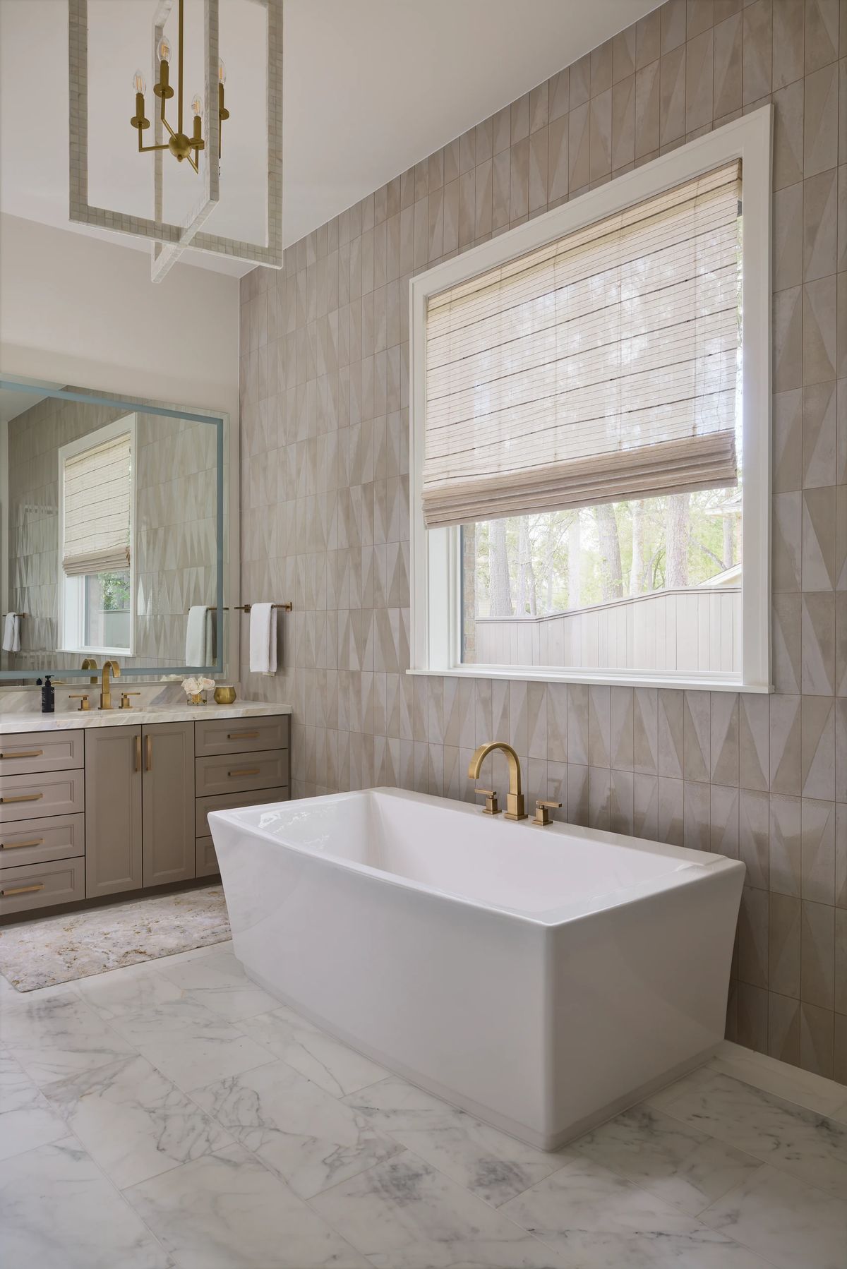 Bathroom with freestanding white bathtub, beige cabinets, geometric wall pattern, and marble floor.