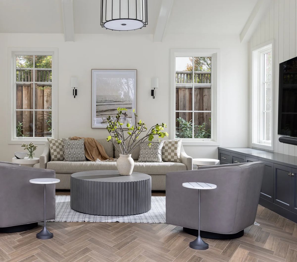 Living room with gray sectional sofa, round chairs, coffee table, rug, large windows, and mounted television.
