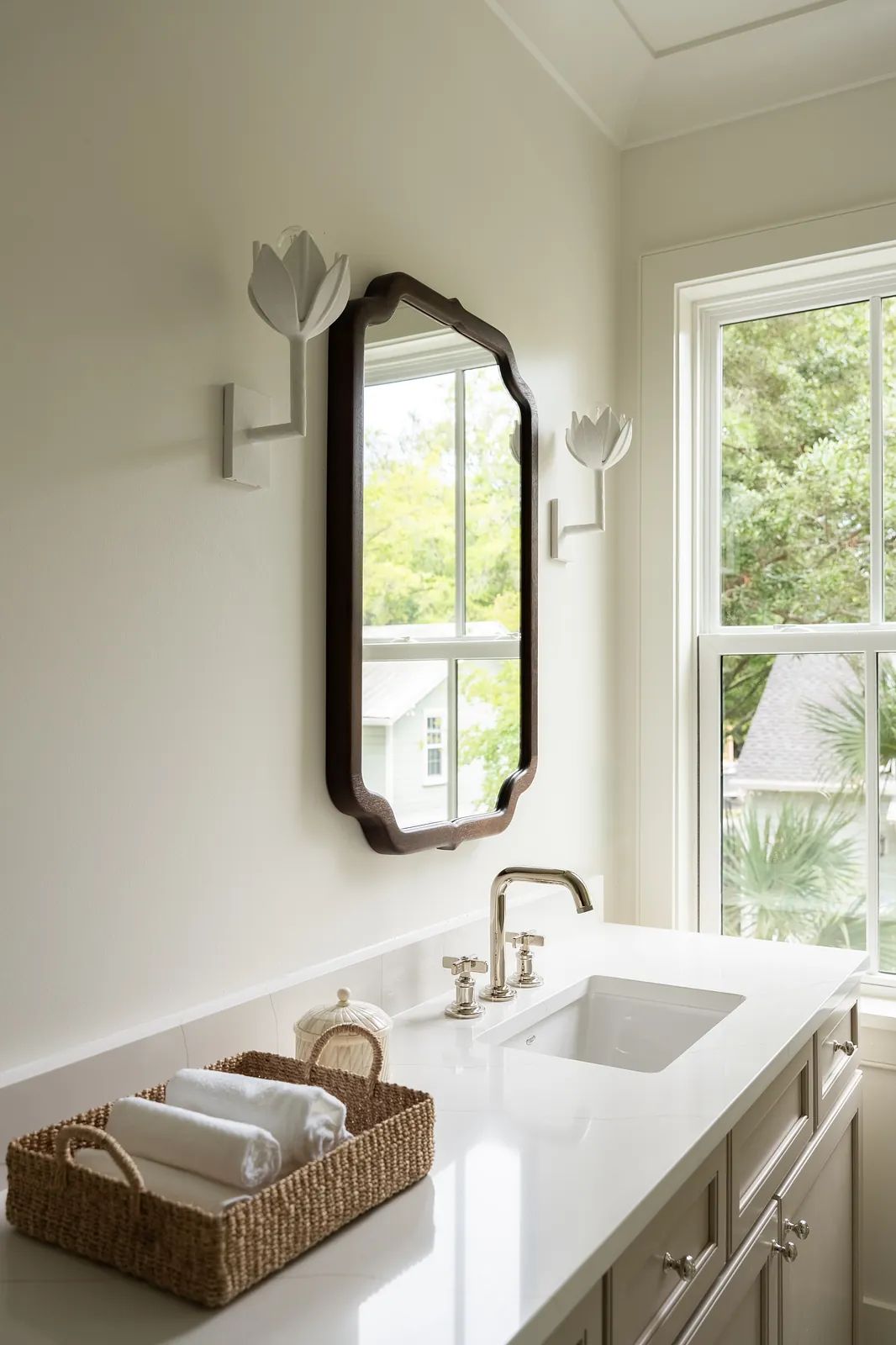 Bathroom with sink, decorative mirror, wall-mounted fixtures, and basket of rolled towels.