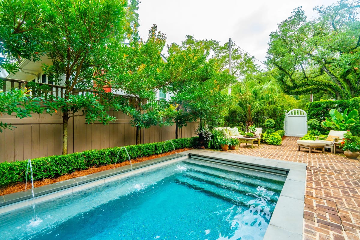 Outdoor patio with swimming pool, surrounding greenery, lounge chairs, and a white gate.