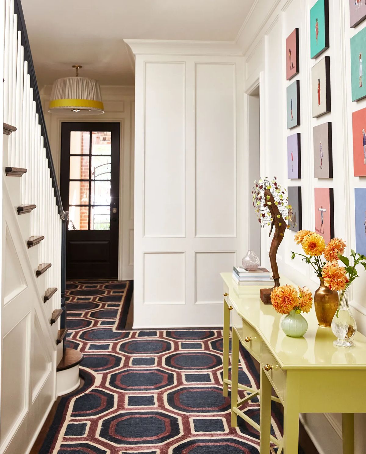 Foyer with green console table, floral arrangements, artwork, patterned rug, and black entrance door.