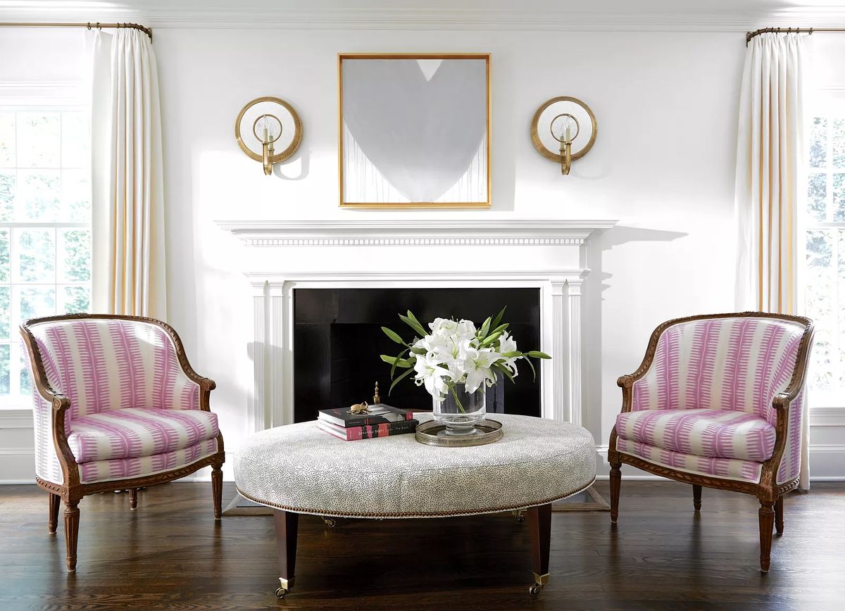 Living room with pink striped chairs, round coffee table, floral centerpiece, and black fireplace with white mantel.