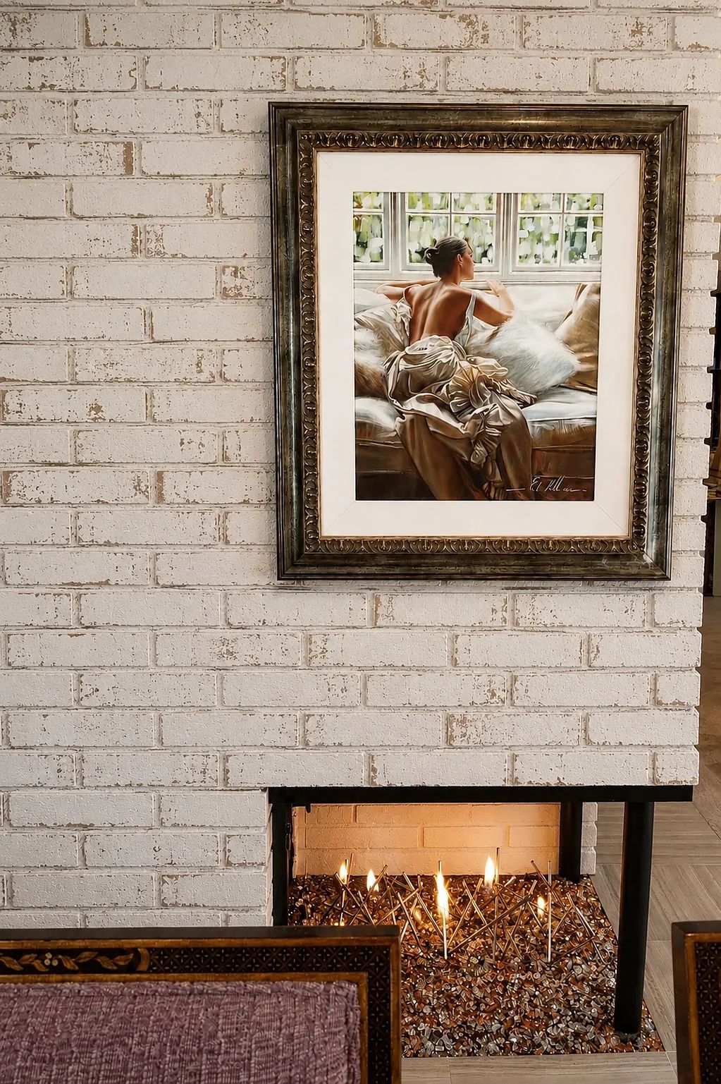 Living room with framed artwork, white brick wall, fireplace with flames, and nearby sofa.