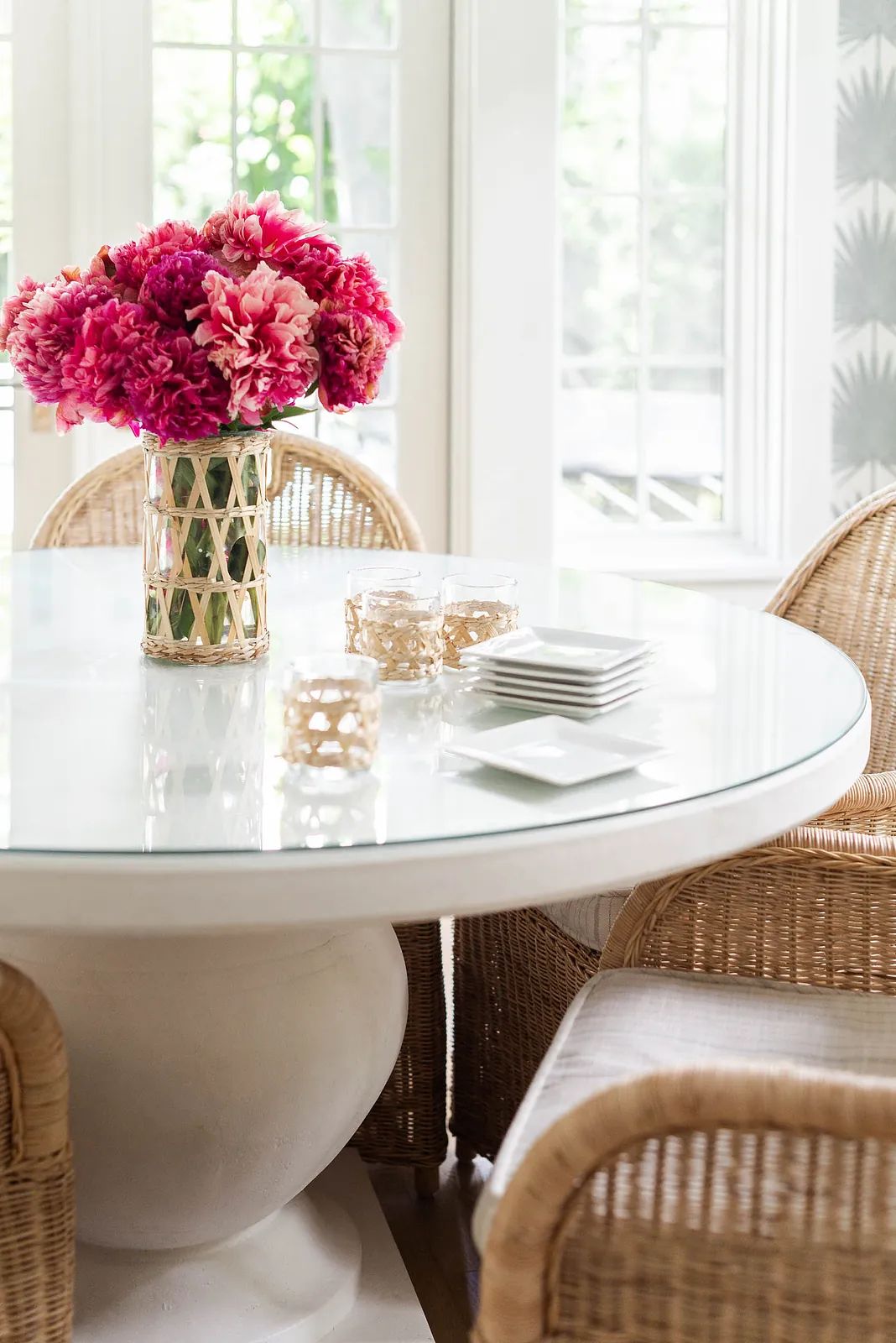 Dining room with round glass table, wicker chairs, pink flower vase, and decorative items