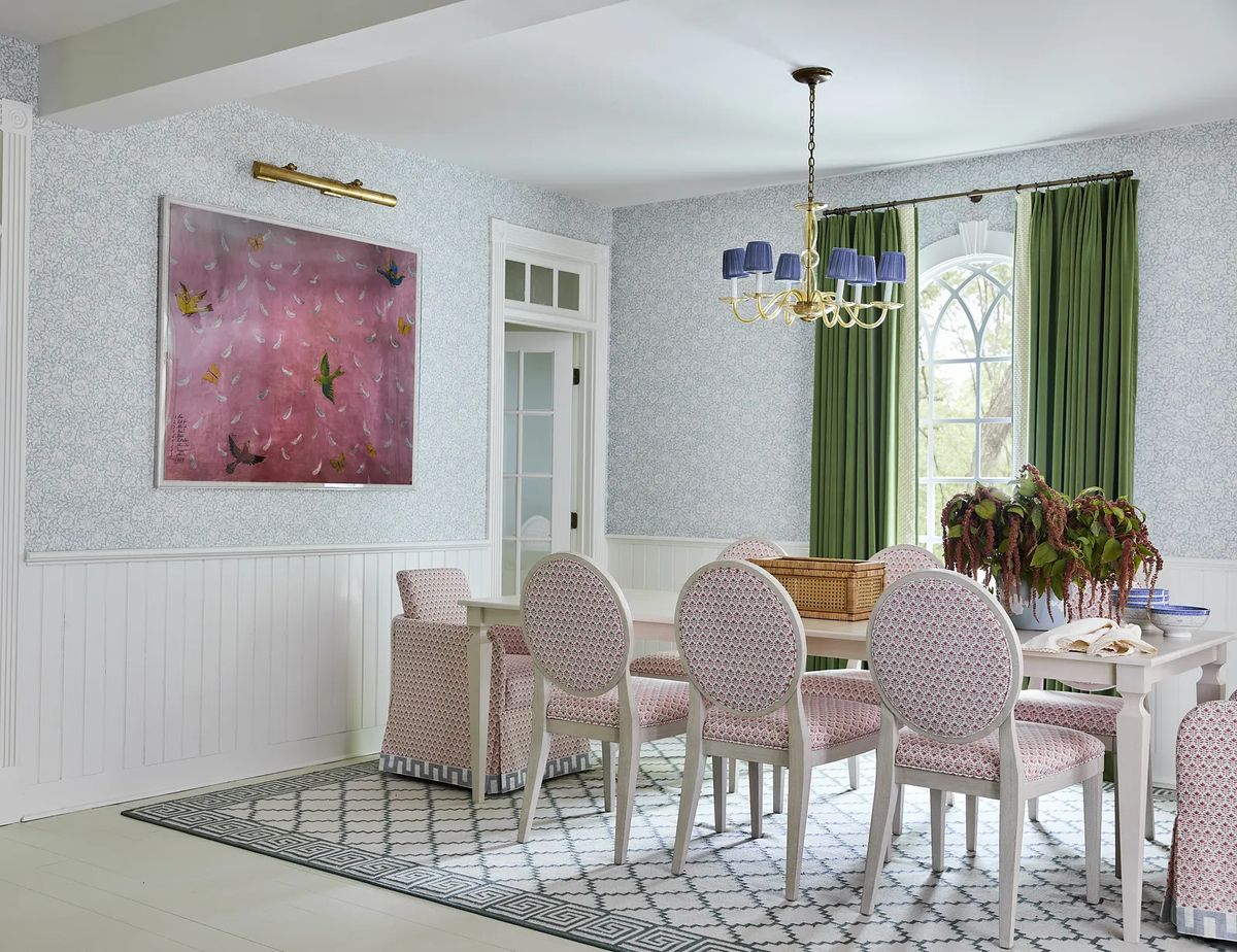Dining room with white table, six upholstered chairs, green curtains, floral wallpaper, and geometric rug.