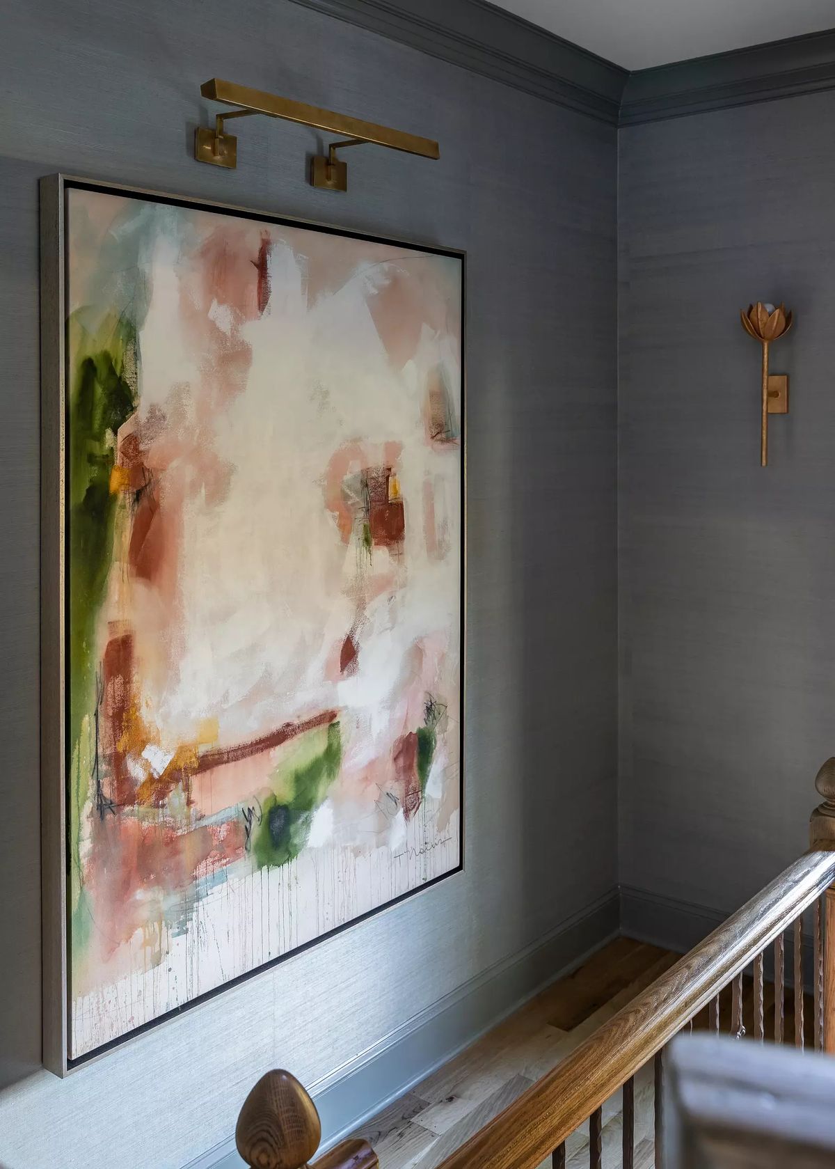 Hallway with abstract painting, wall sconce, light wood floor, and wooden railing
