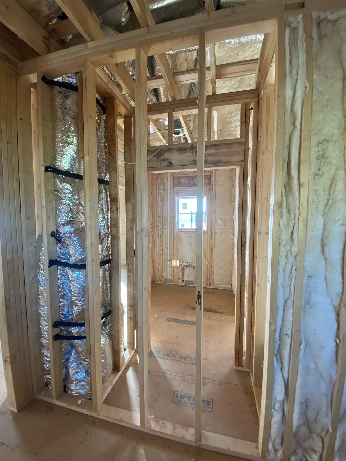 Unfinished space with exposed wooden framing, insulation, and a window opening.
