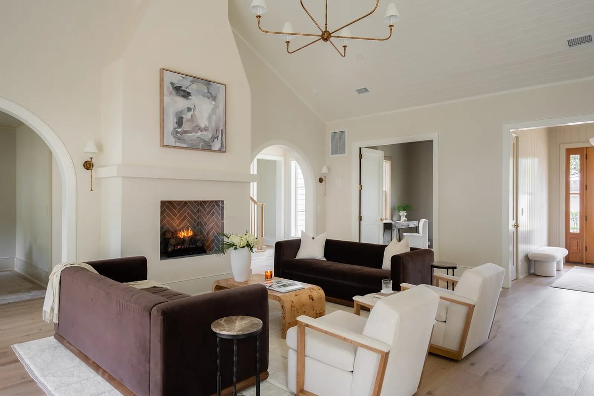 Living room with dark brown sofas, light area rug, coffee table, white armchairs, and herringbone fireplace.
