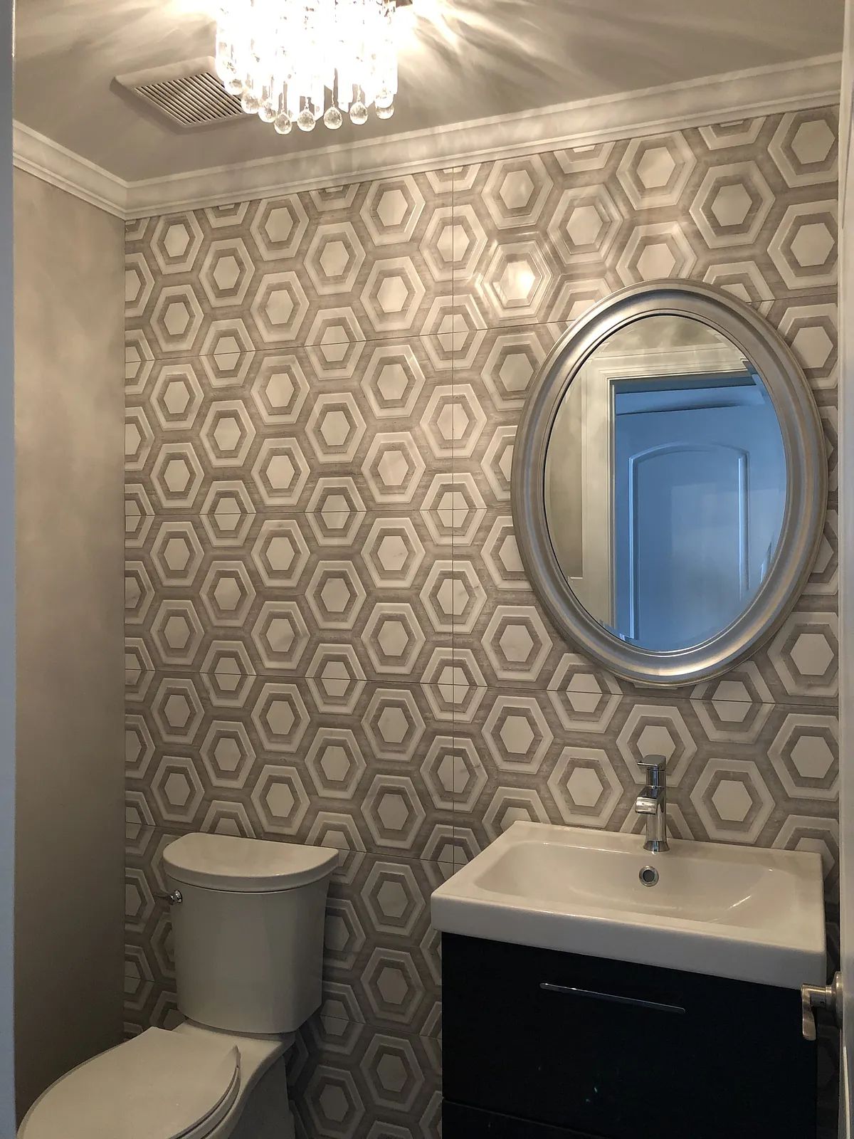 Powder room with hexagonal wallpaper, round mirror, black vanity, sink, and white toilet.