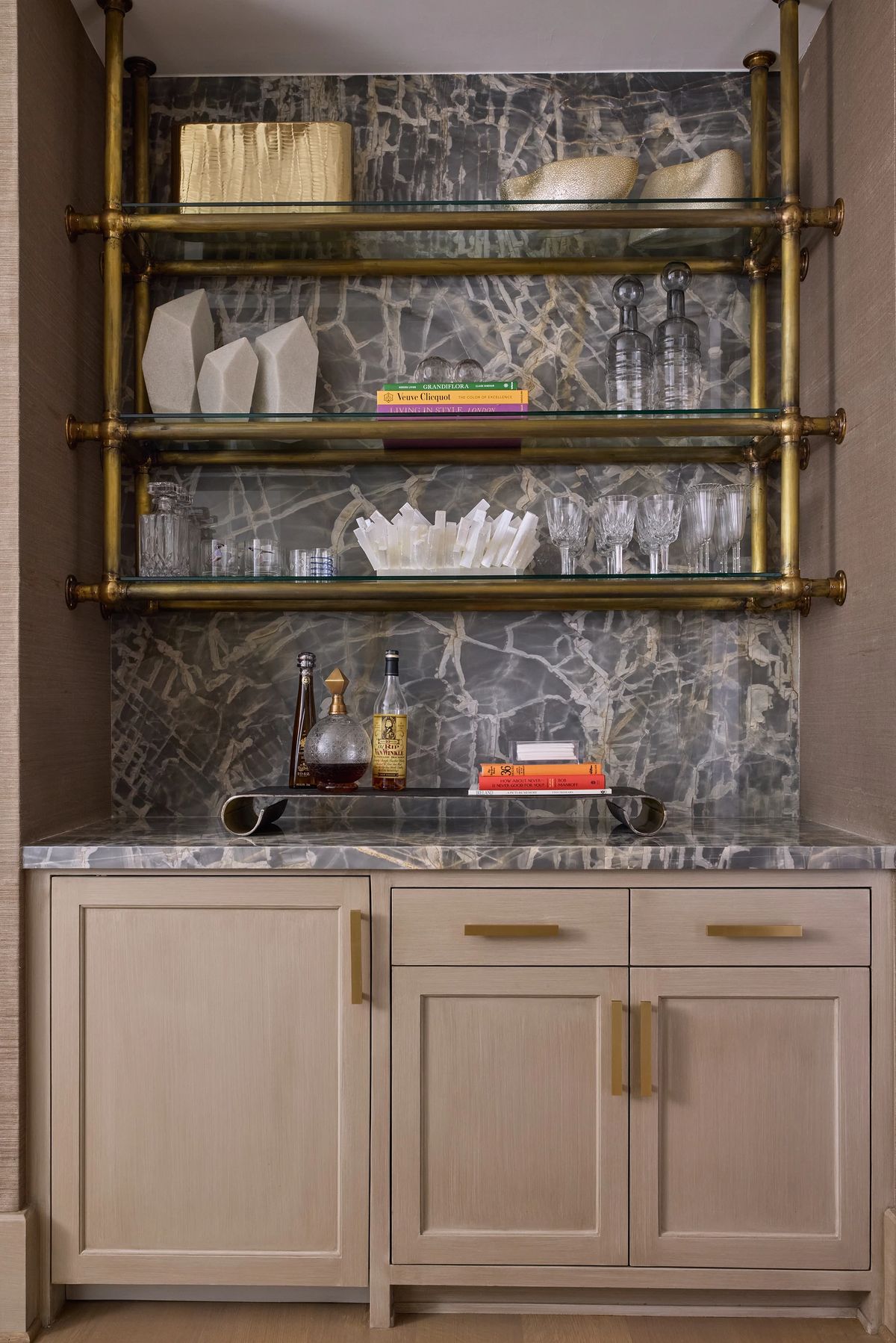 Storage area with open shelving, glassware, decorative bottles, and cabinet doors with brass handles.