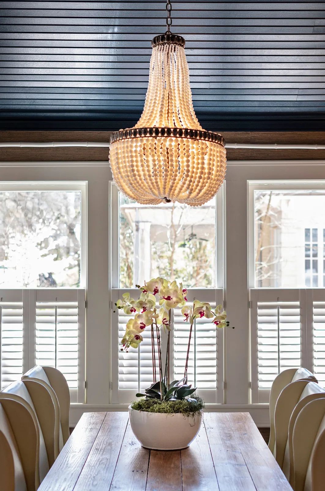 Dining room with wooden table, upholstered chairs, chandelier, and decorative flower arrangement.