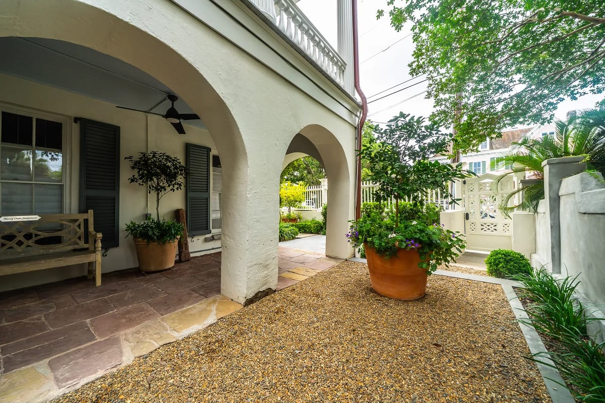 Exterior front area with stone path, potted plant, bench, and arched entryways.