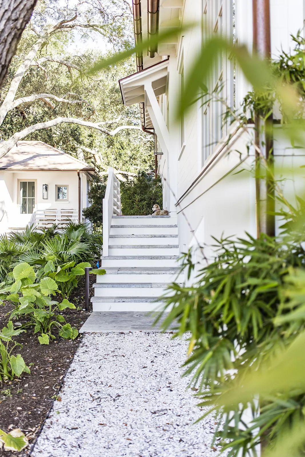Exterior front view with white steps, greenery, gravel, and a light-colored house facade.