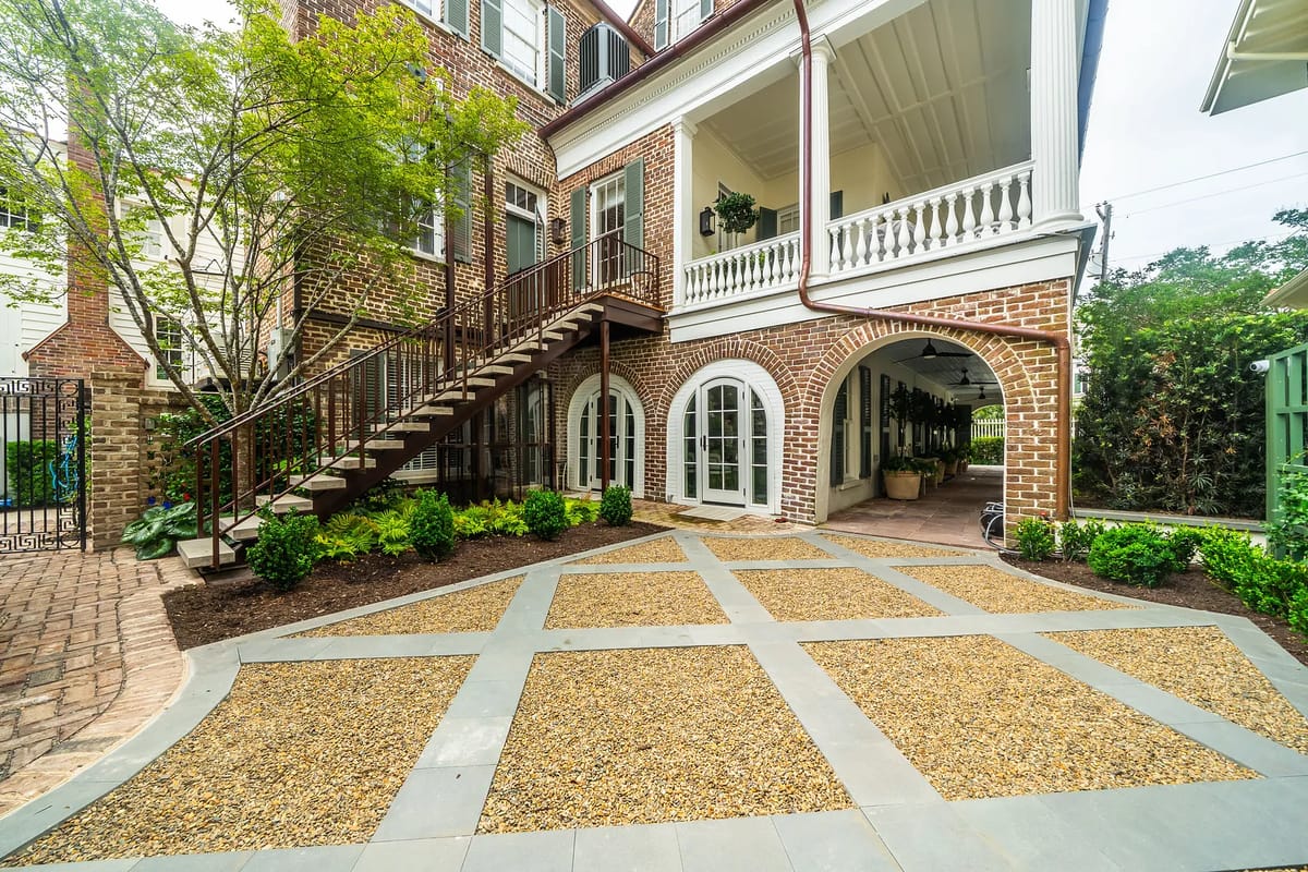 Exterior rear space with brick building, staircase, gravel area, and landscaped shrubs.