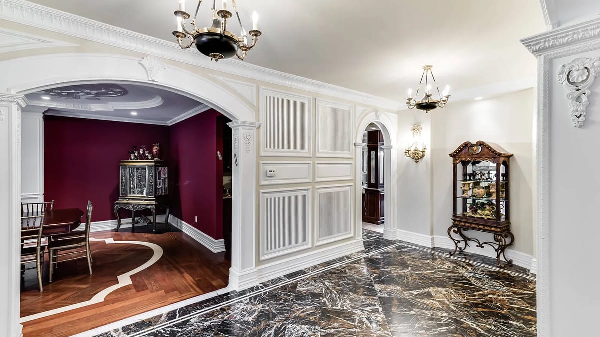 Foyer with marble floor, arched entryways, wall paneling, and chandeliers leading to a dining area.