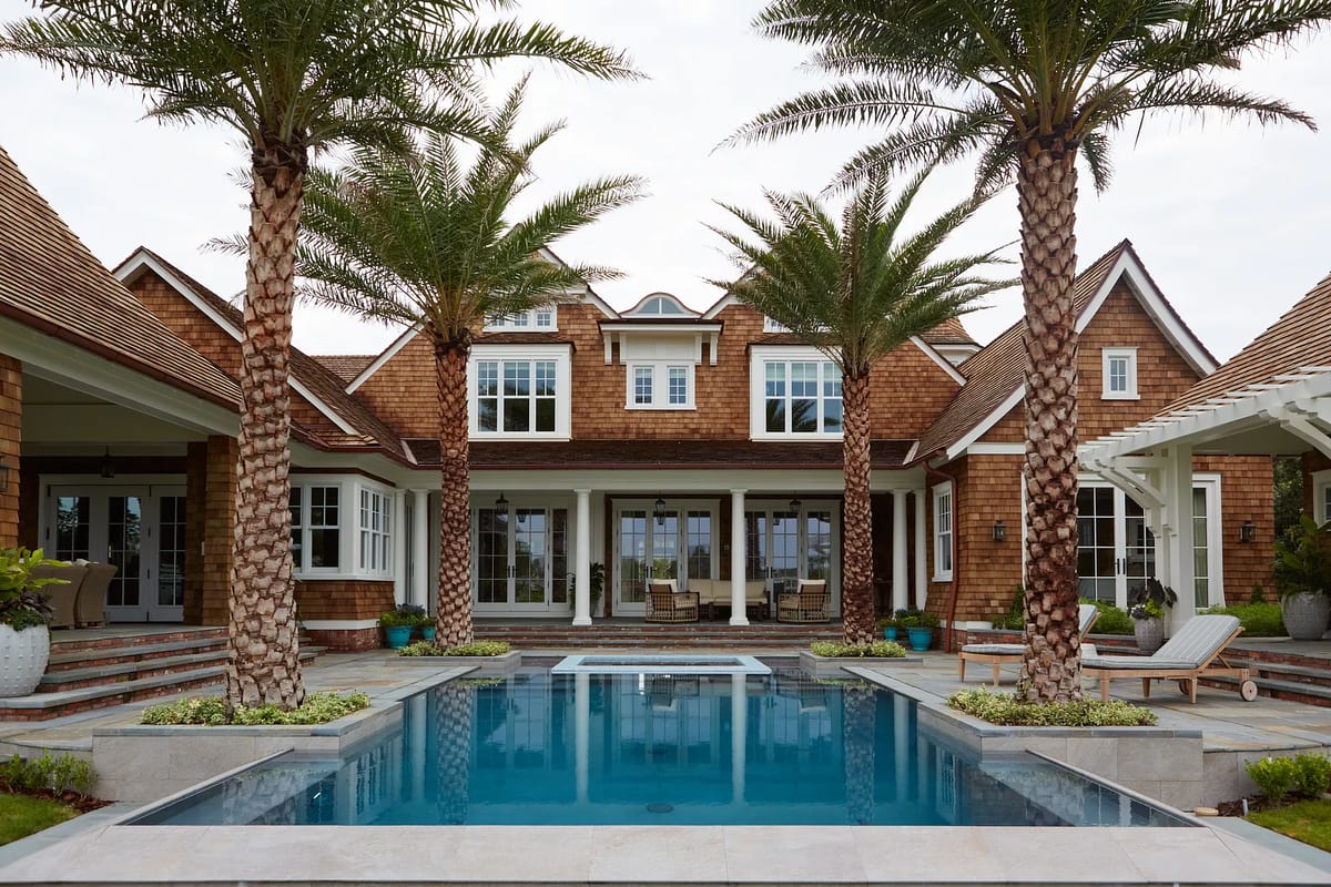 Exterior rear area with pool, palm trees, pavers, and a two-story house with large windows.