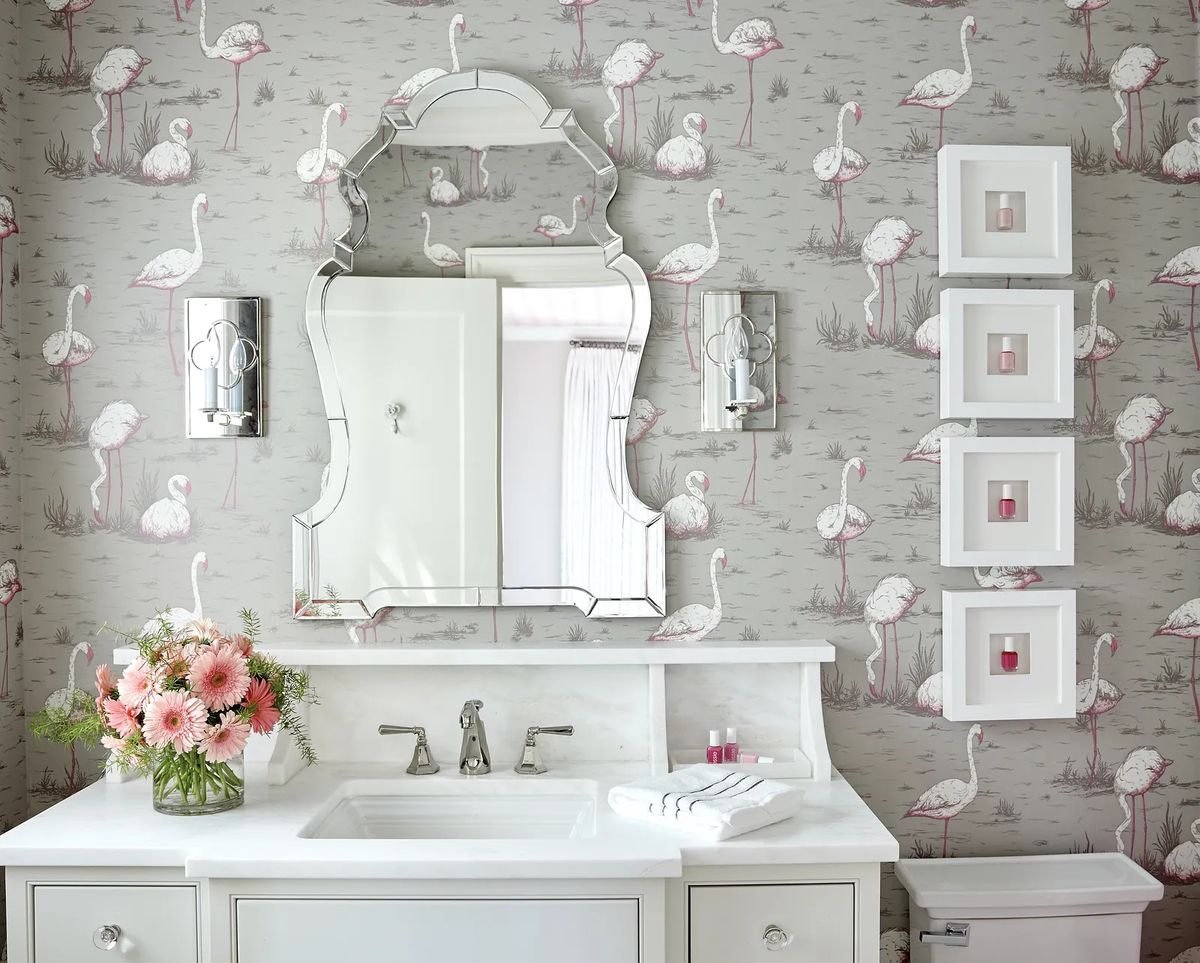 Bathroom with marble sink countertop, flamingo wallpaper, floral sconces, and framed artwork.