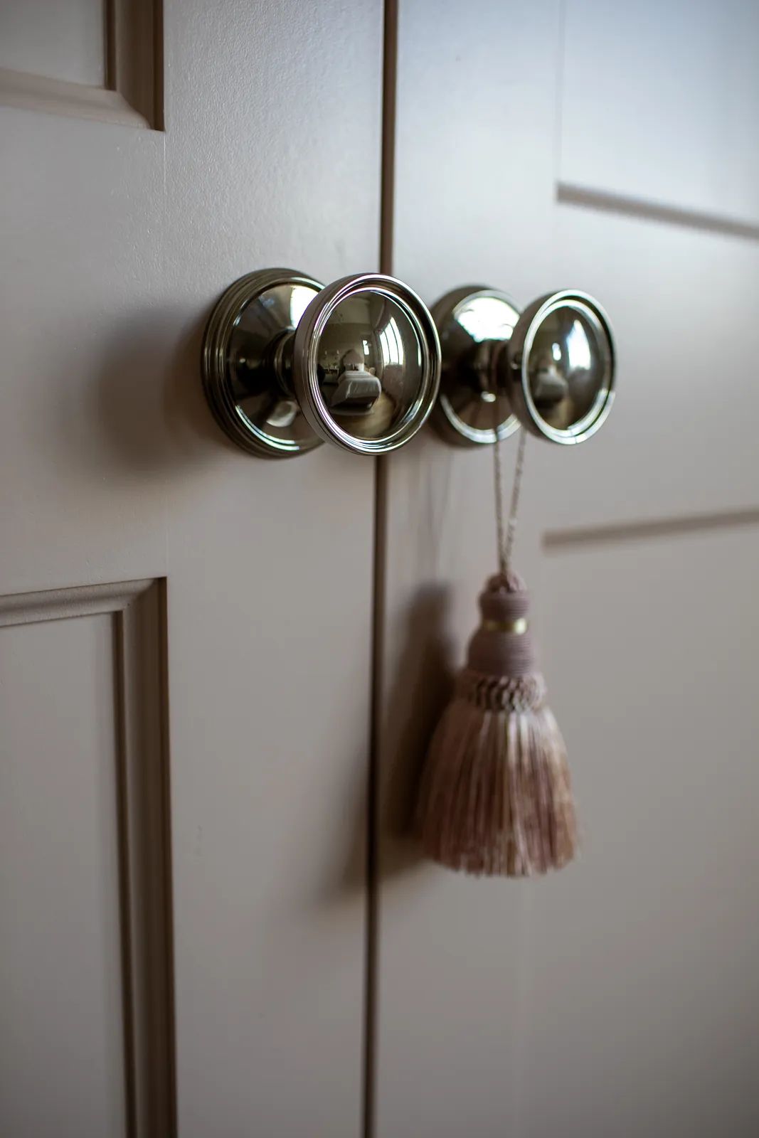 Close-up of cabinet doors with three metal knobs and a decorative tassel in light beige color.