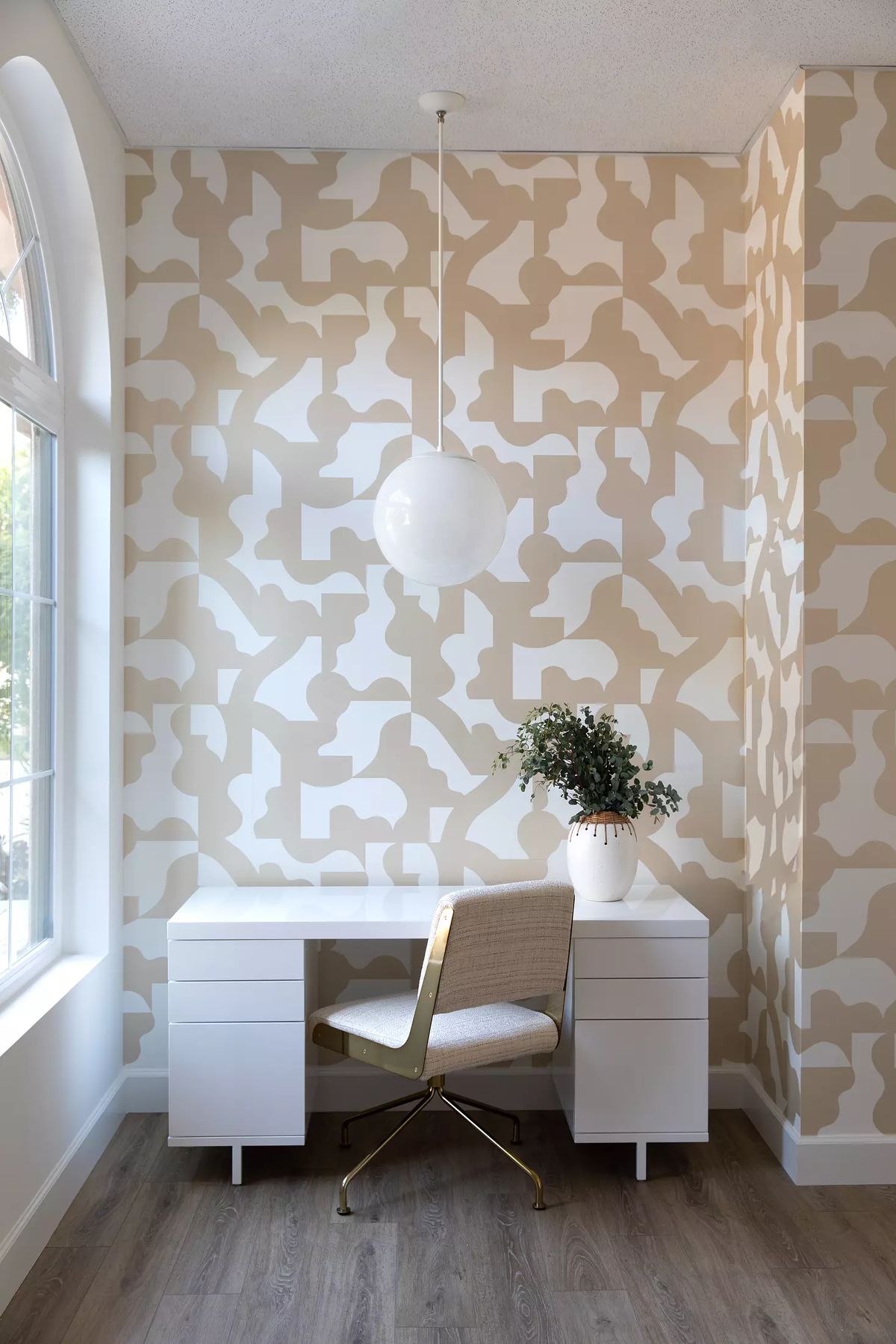 Office with white desk, gold chair, abstract wallpaper, and small plant in a vase