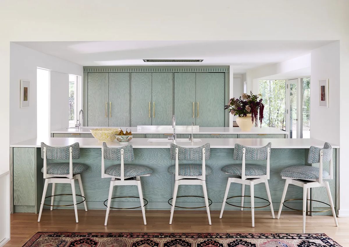 Kitchen with light blue cabinetry, white countertops, bar stools, sink, and decorative flowers.