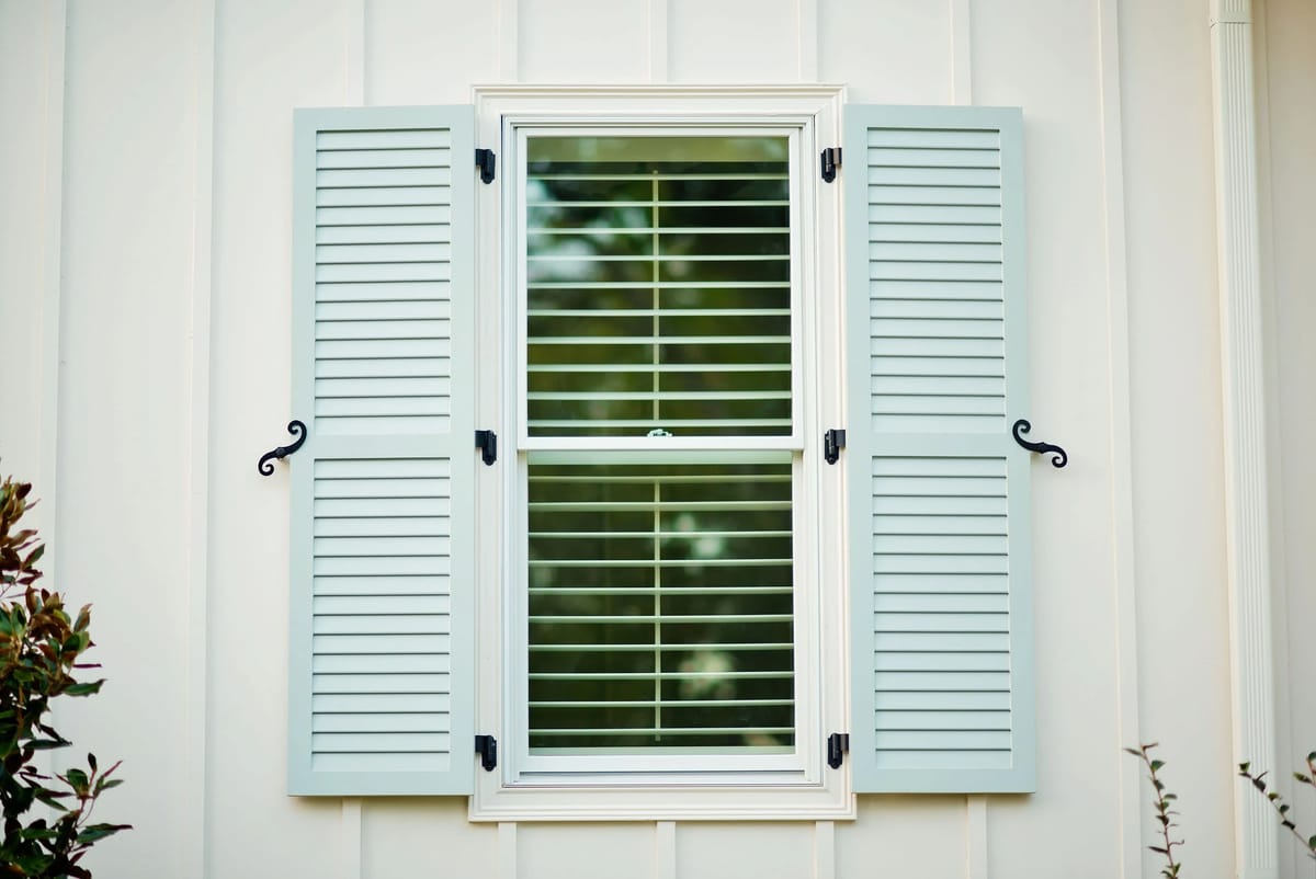 Window with light green shutters, white wall, and horizontal blinds.