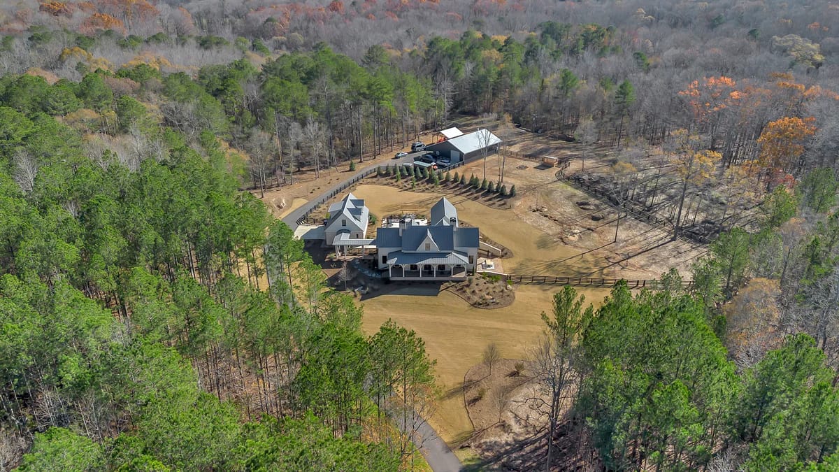 Aerial view of a large estate with multi-level home, porches, trees, and landscaped areas.