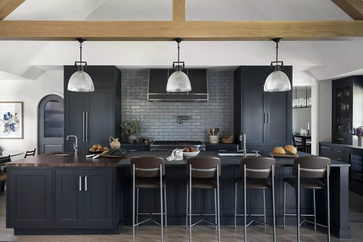 Kitchen with dark cabinets, central island, bar stools, glass pendant lights, and patterned gray backsplash.