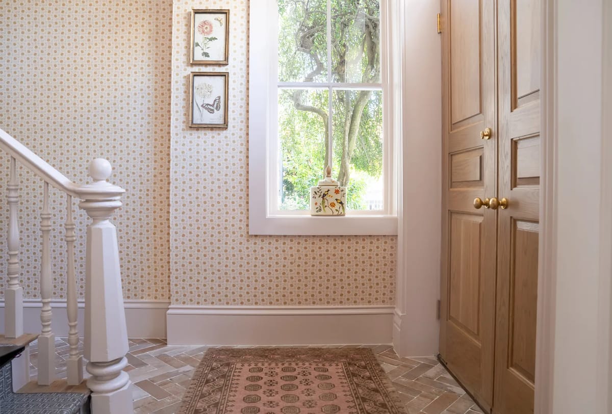 Foyer with patterned wallpaper, wooden door, area rug, staircase, framed artworks, and decorative box