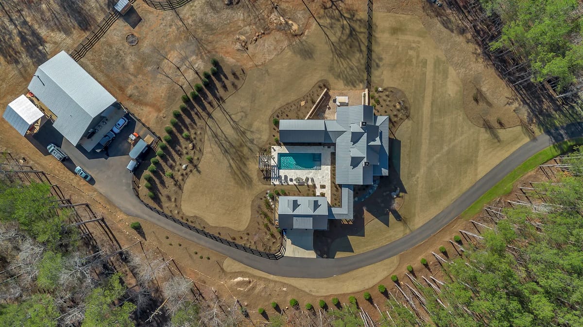 Aerial view of a residential property with main house, swimming pool, patio, and landscaped surroundings.
