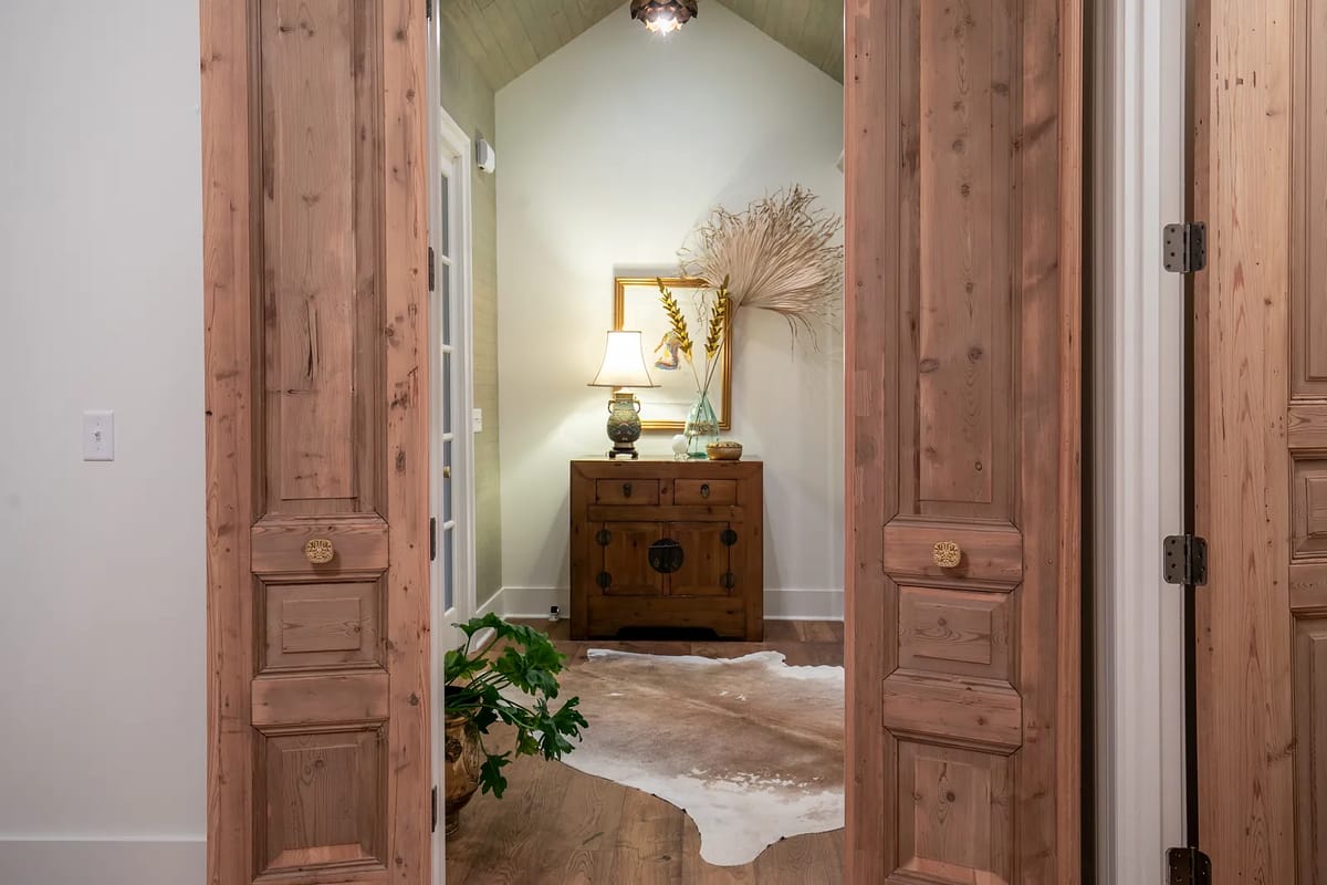Foyer with wooden chest, table lamp, decorative vase, mirror, and cowhide rug.