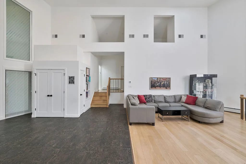 Living room with gray sectional sofa, coffee table, artwork, and large windows with a staircase.