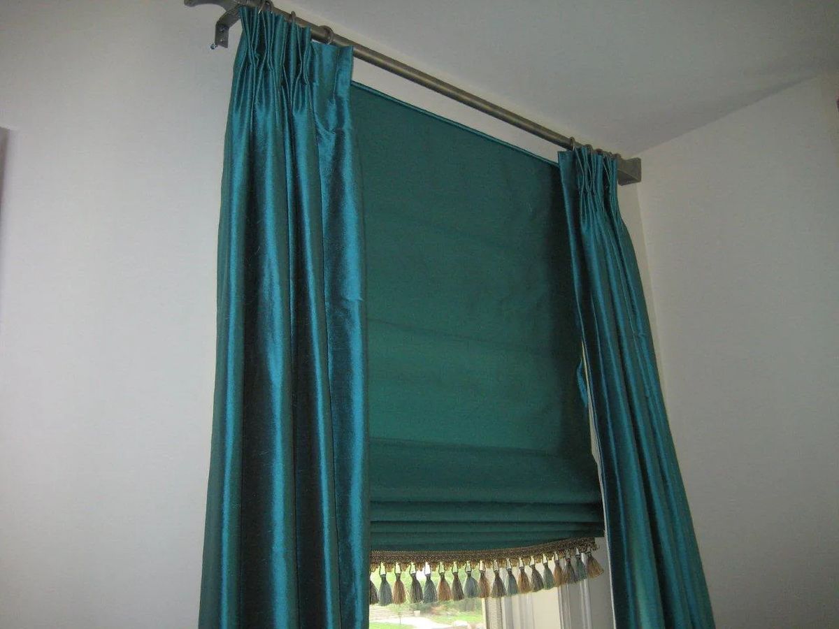 Teal window treatment with curtains and roller shade featuring tassels.
