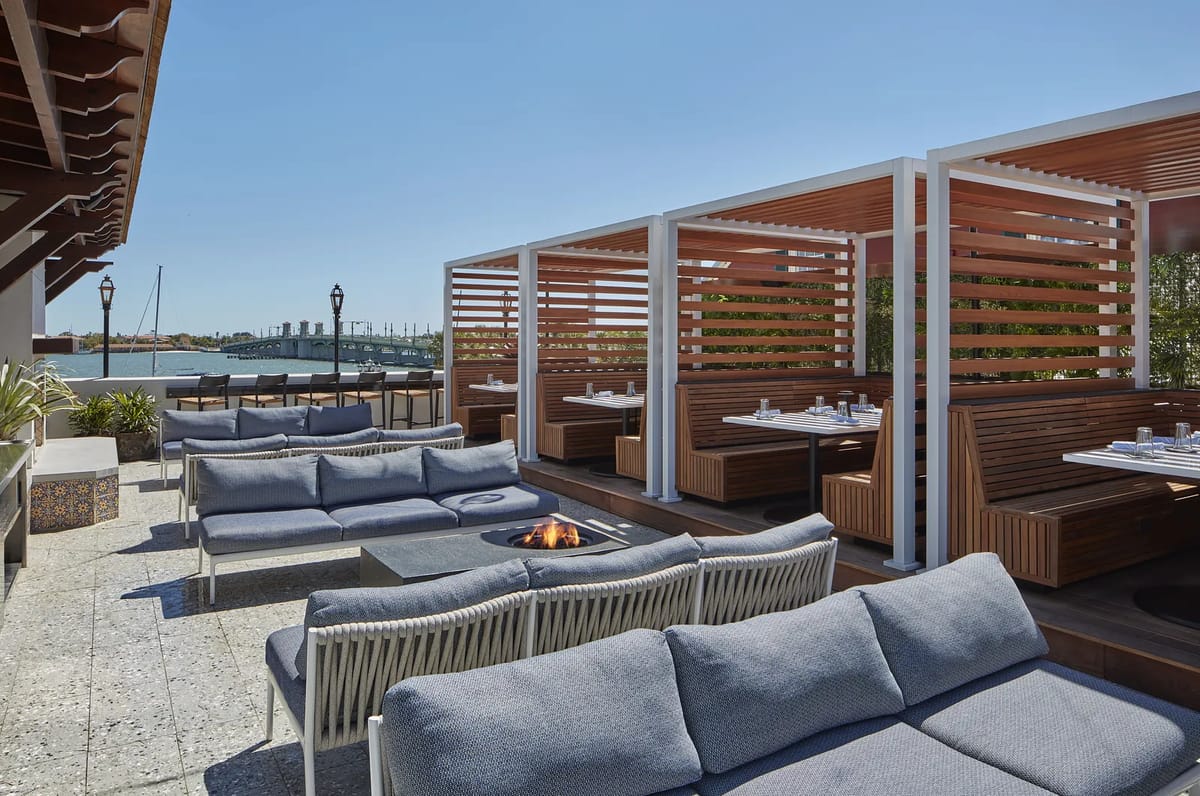 Patio with sectional sofas, fire pit, dining areas, slatted wood partitions, and planters with greenery.