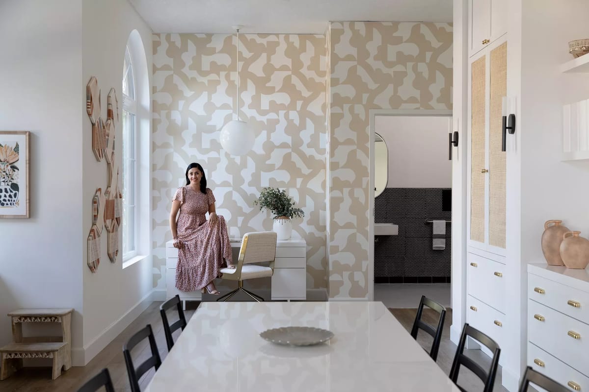 Dining room with black table, chairs, white cabinetry, patterned walls, large window, and decorative vases.