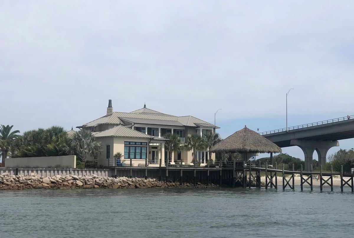 Exterior view of a waterfront house with gazebo, large windows, and palm trees, located on a dock.