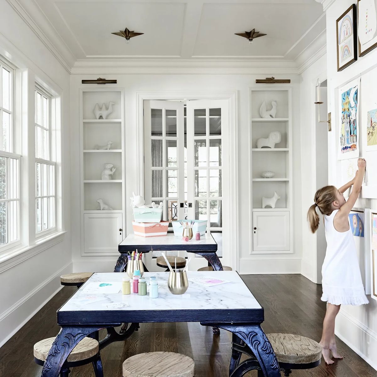 Room with marble table, round stools, built-in shelves, and child hanging artwork.