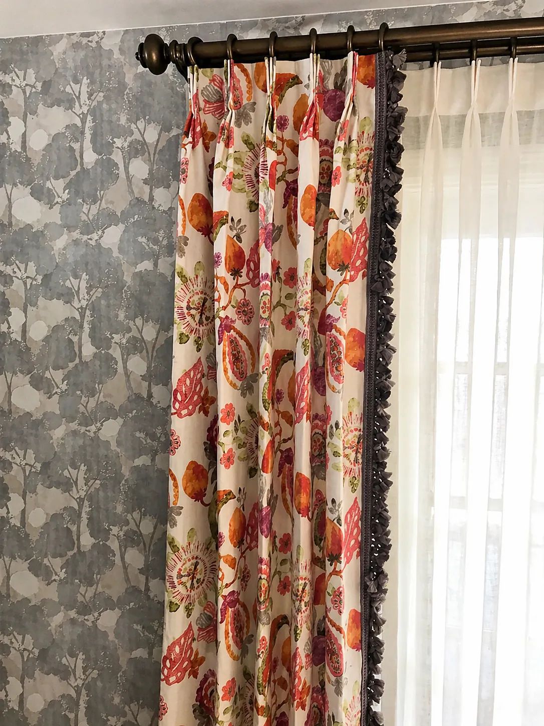 Wall with floral-patterned curtains, sheer white layer, and blue leaf-patterned wallpaper.