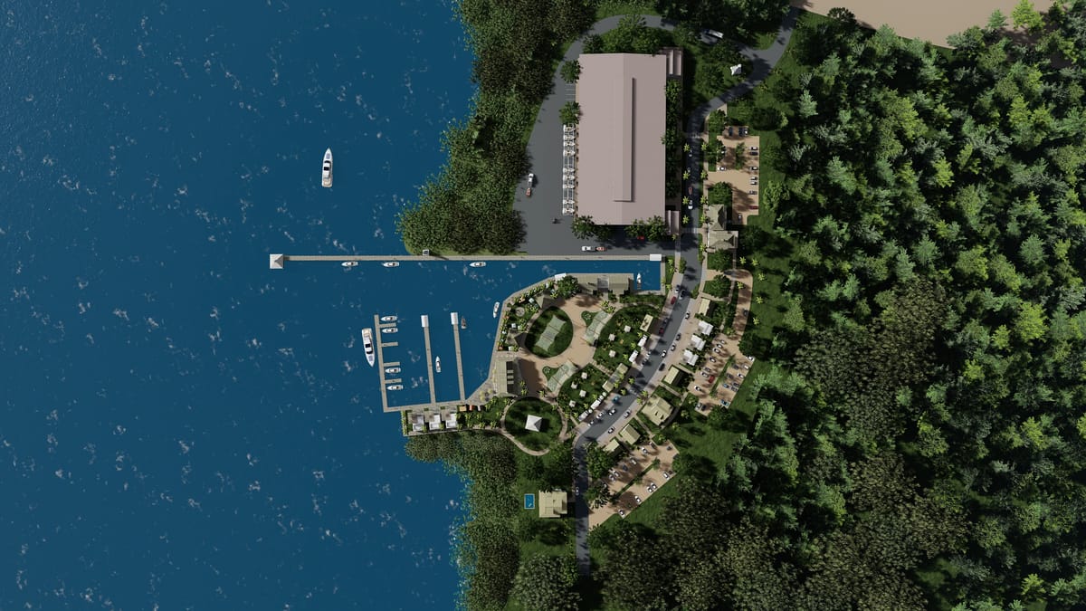 Aerial view of a marina with boats, dock, and wooded shoreline with adjacent buildings.