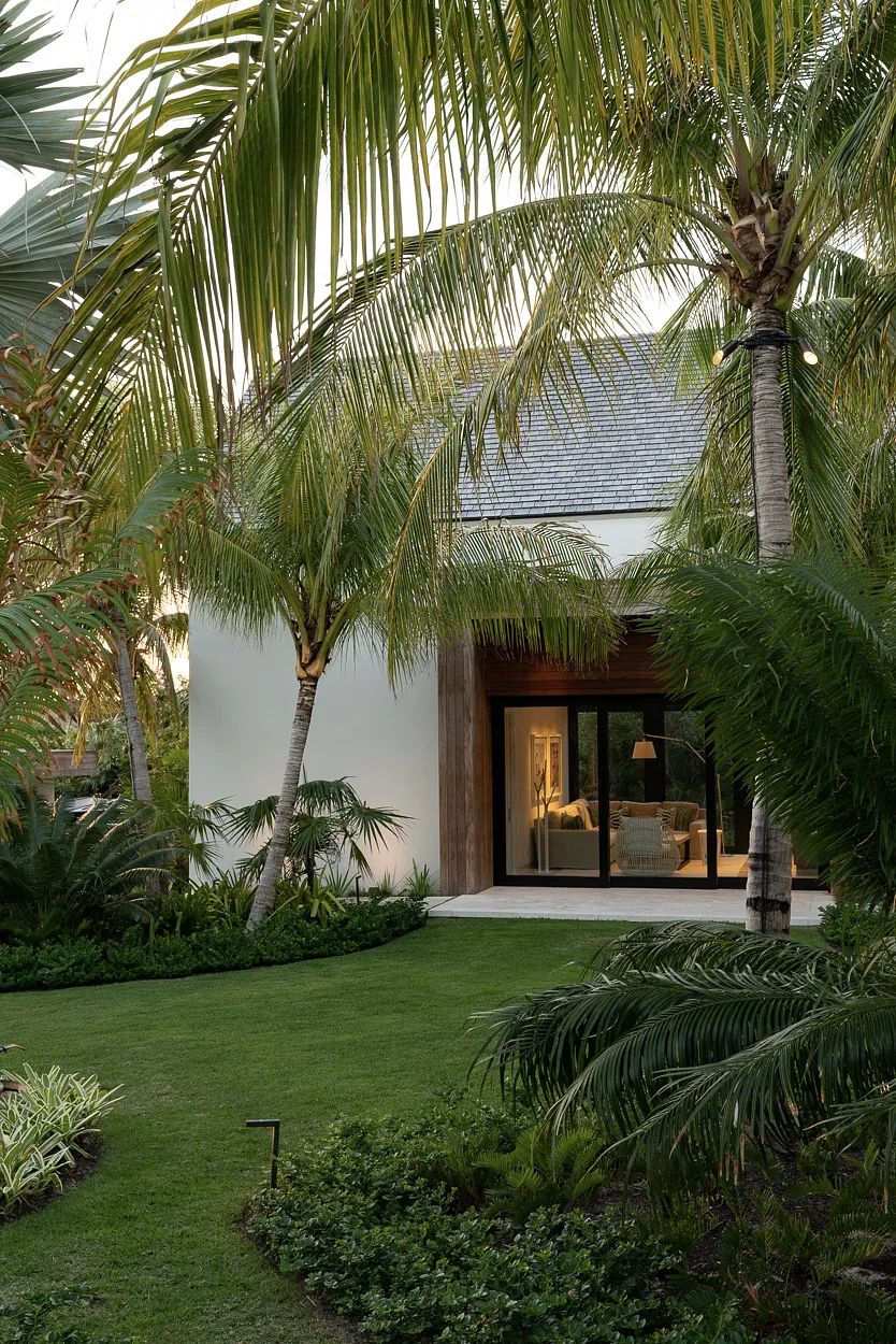 Exterior front view with a house featuring large glass doors, palm trees, and a manicured lawn.
