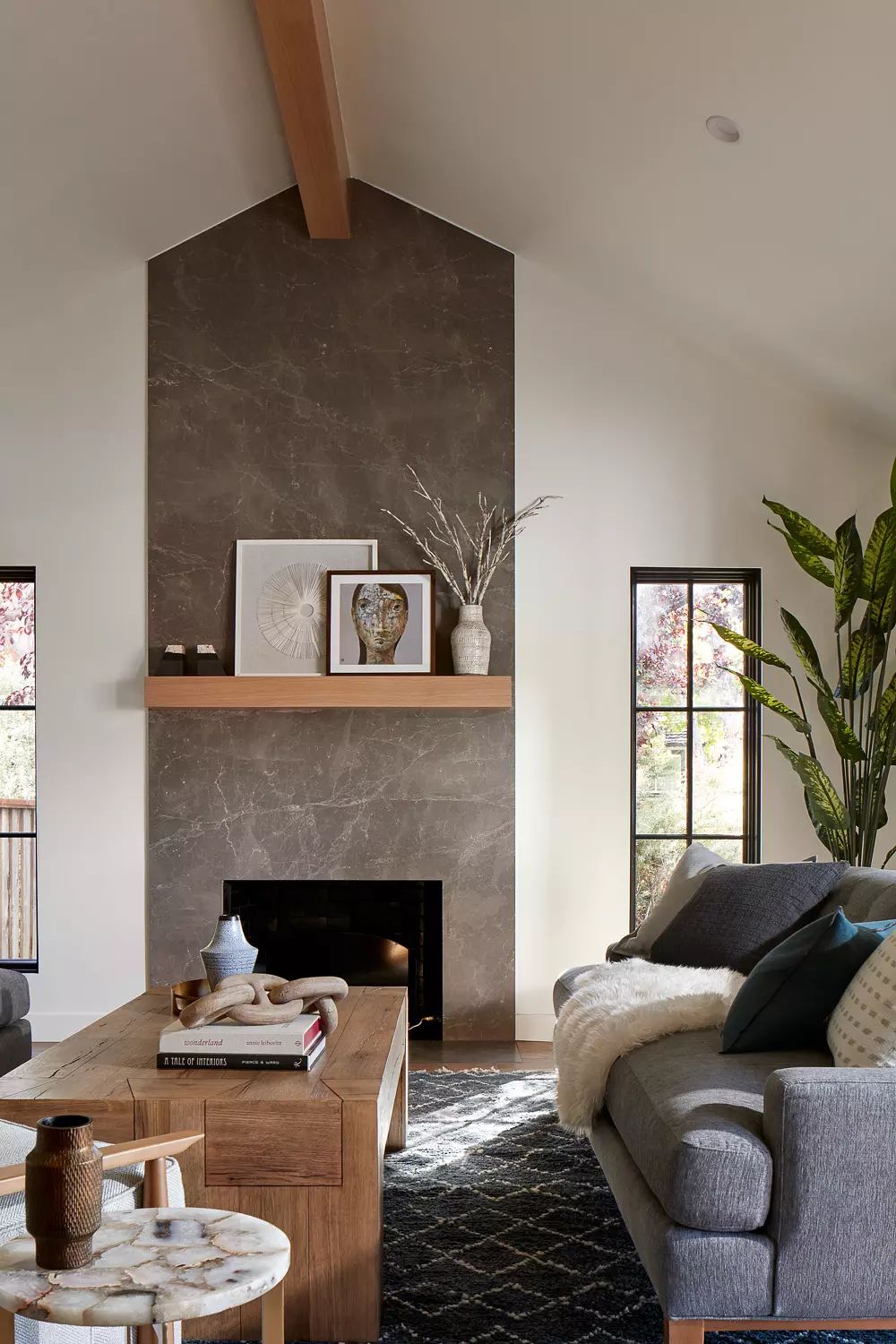 Living room with gray sofa, wooden coffee table, area rug, stone accent wall, and large windows
