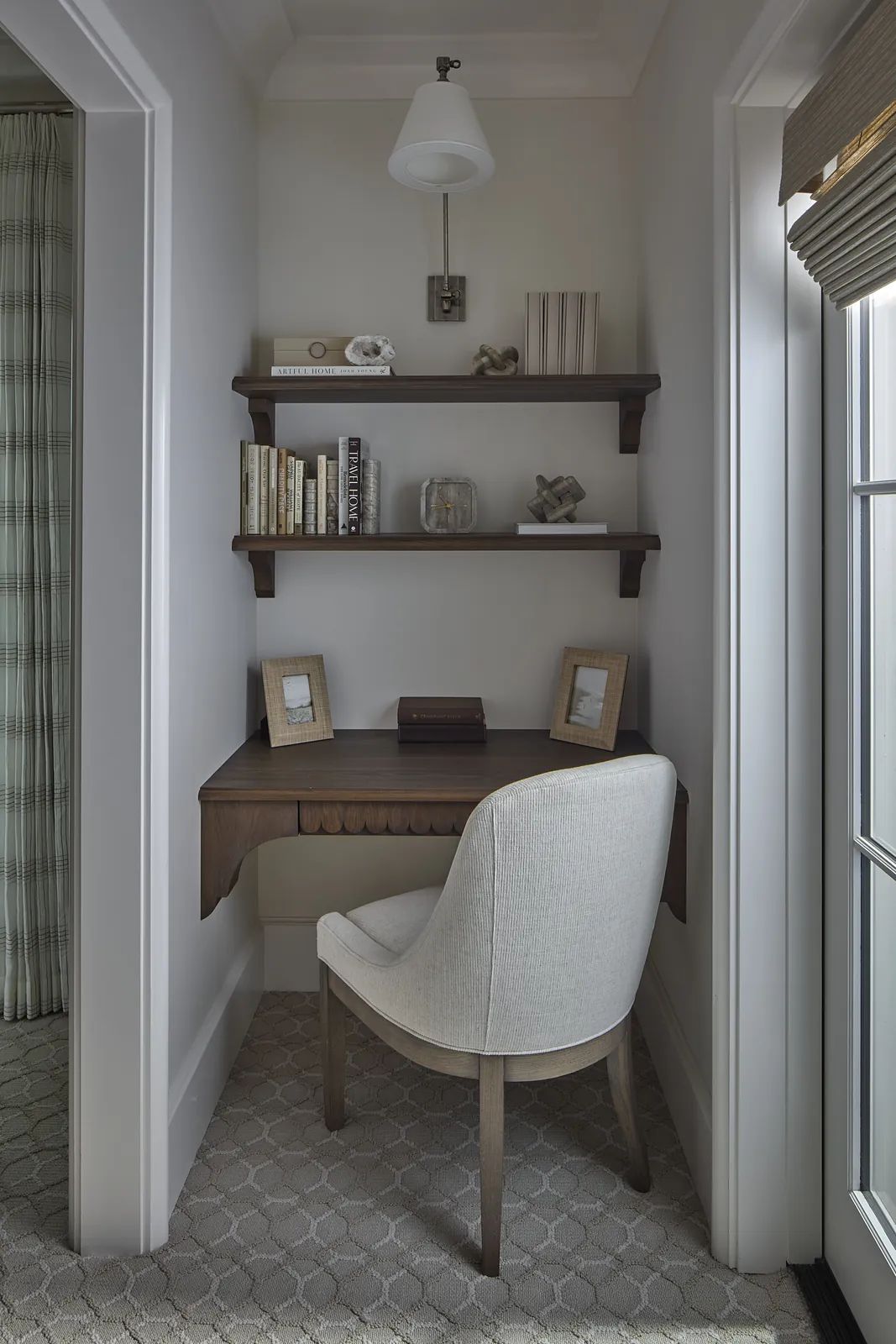 Office nook with wooden desk, gray chair, wall-mounted shelves, books, and framed pictures.