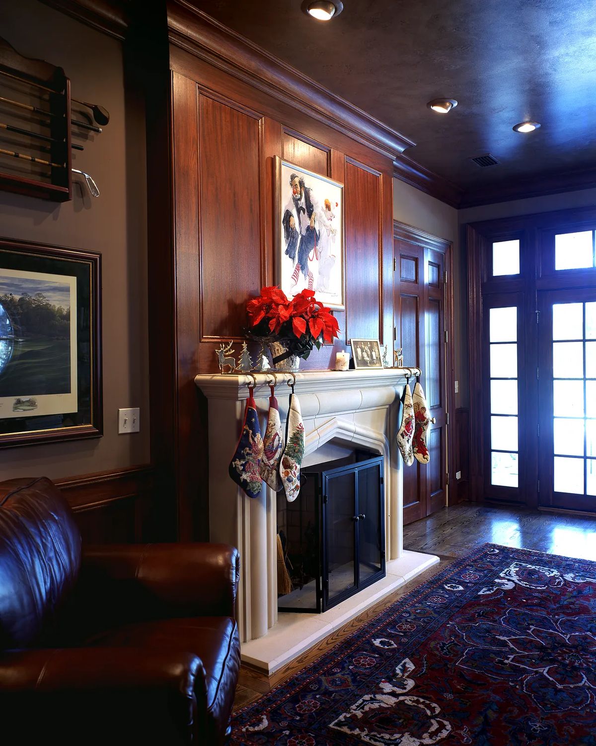 Living room with brown leather armchair, white fireplace, framed artwork, and large windows.