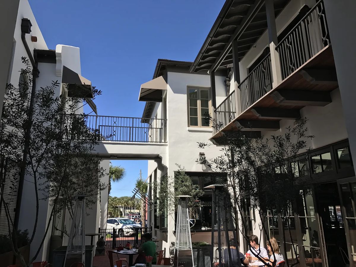 Exterior courtyard with paved floor, outdoor seating, and small trees between buildings.