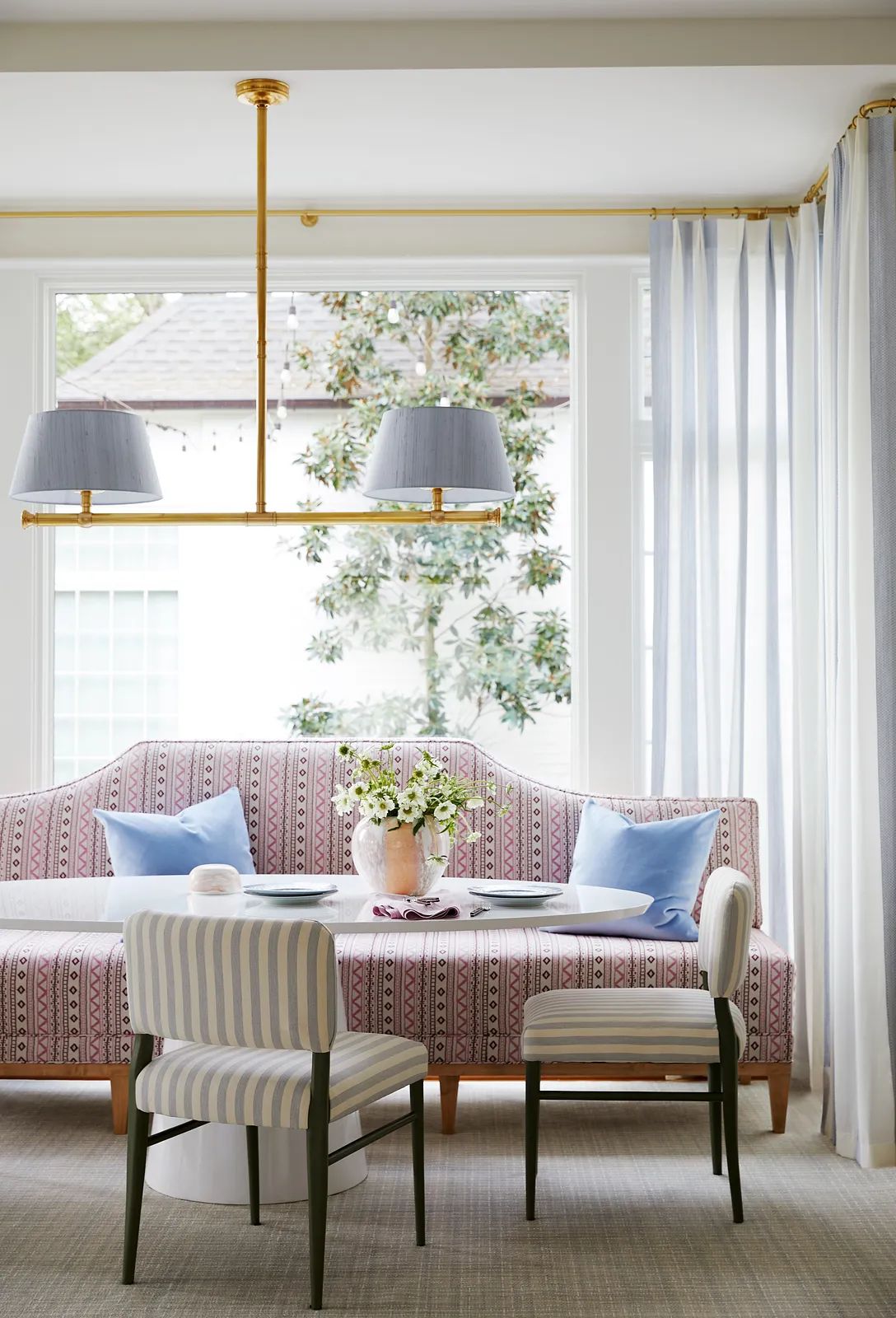 Dining room with patterned banquette, round table, striped chairs, floral centerpiece, and natural light from windows