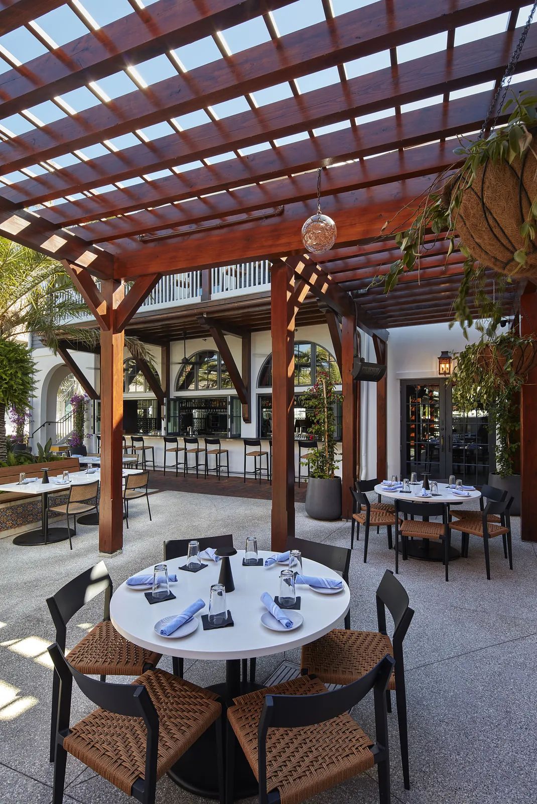 Outdoor dining area with round table, black and woven chairs, and a pergola above.