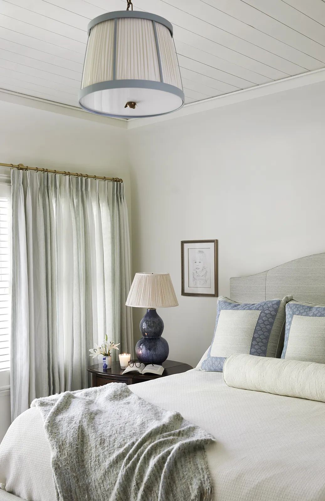 Bedroom with queen bed, nightstand, table lamp, curtains, and framed artwork.
