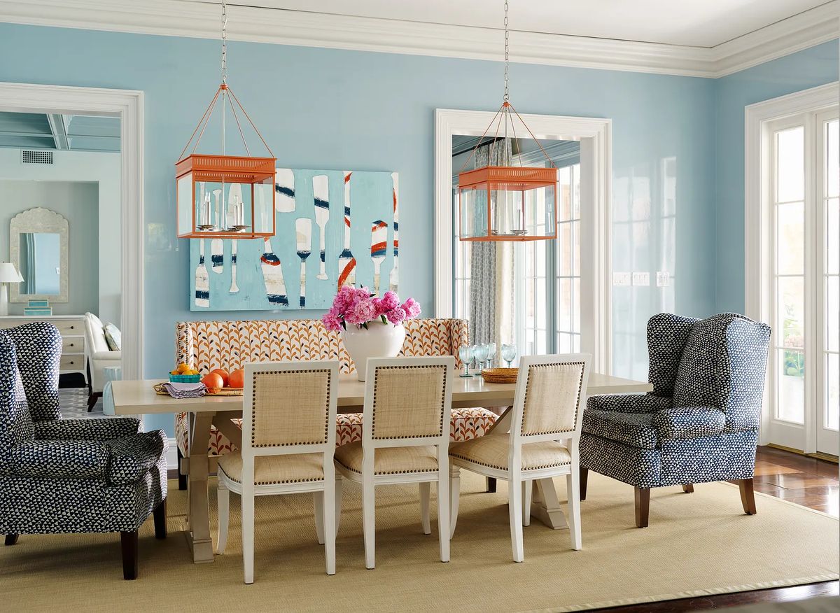 Dining room with a table, patterned chairs, banquette, lanterns, and large artwork on light blue walls.