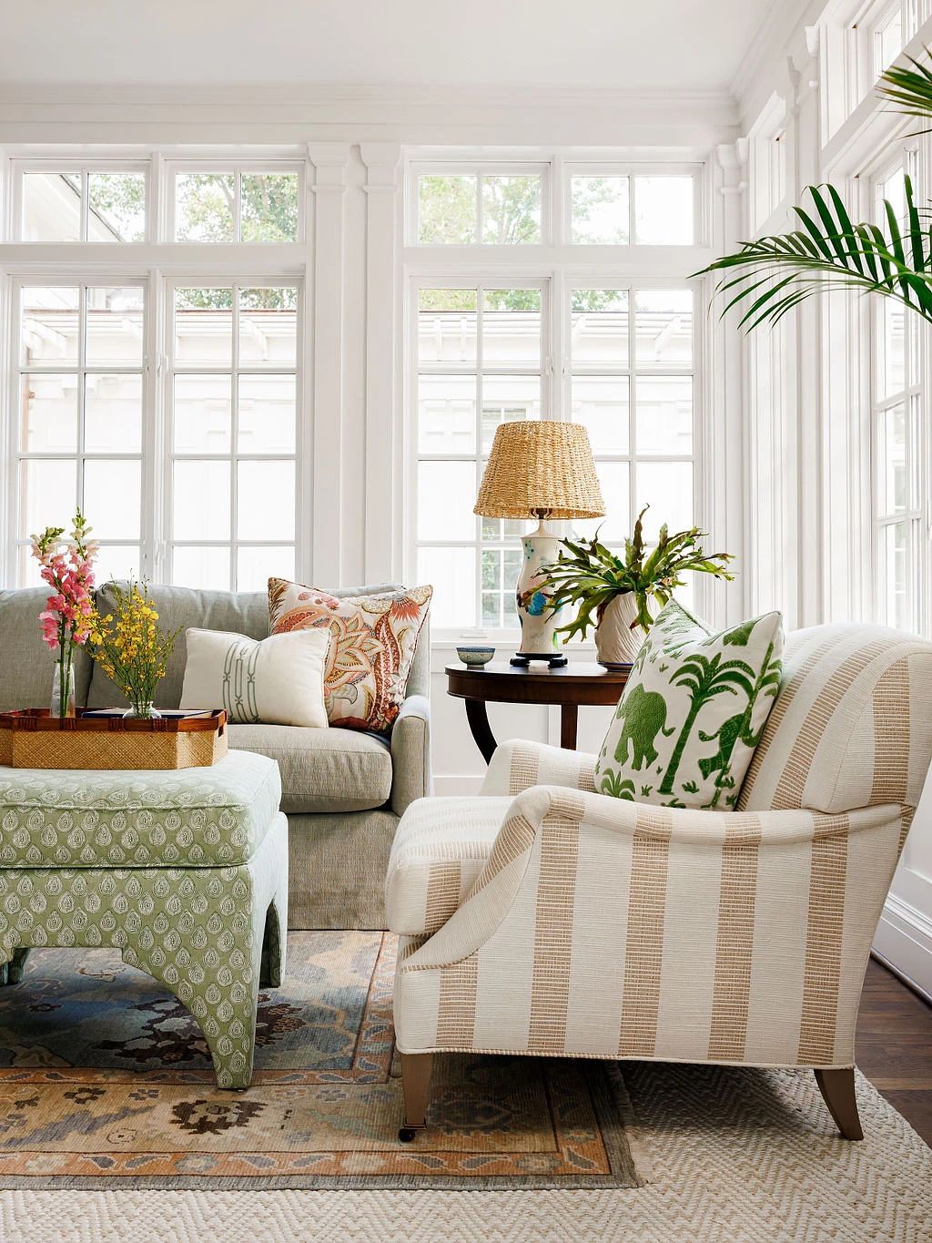 Living room with gray sofa, striped armchair, ottoman, table, lamp, plants, and a patterned rug.