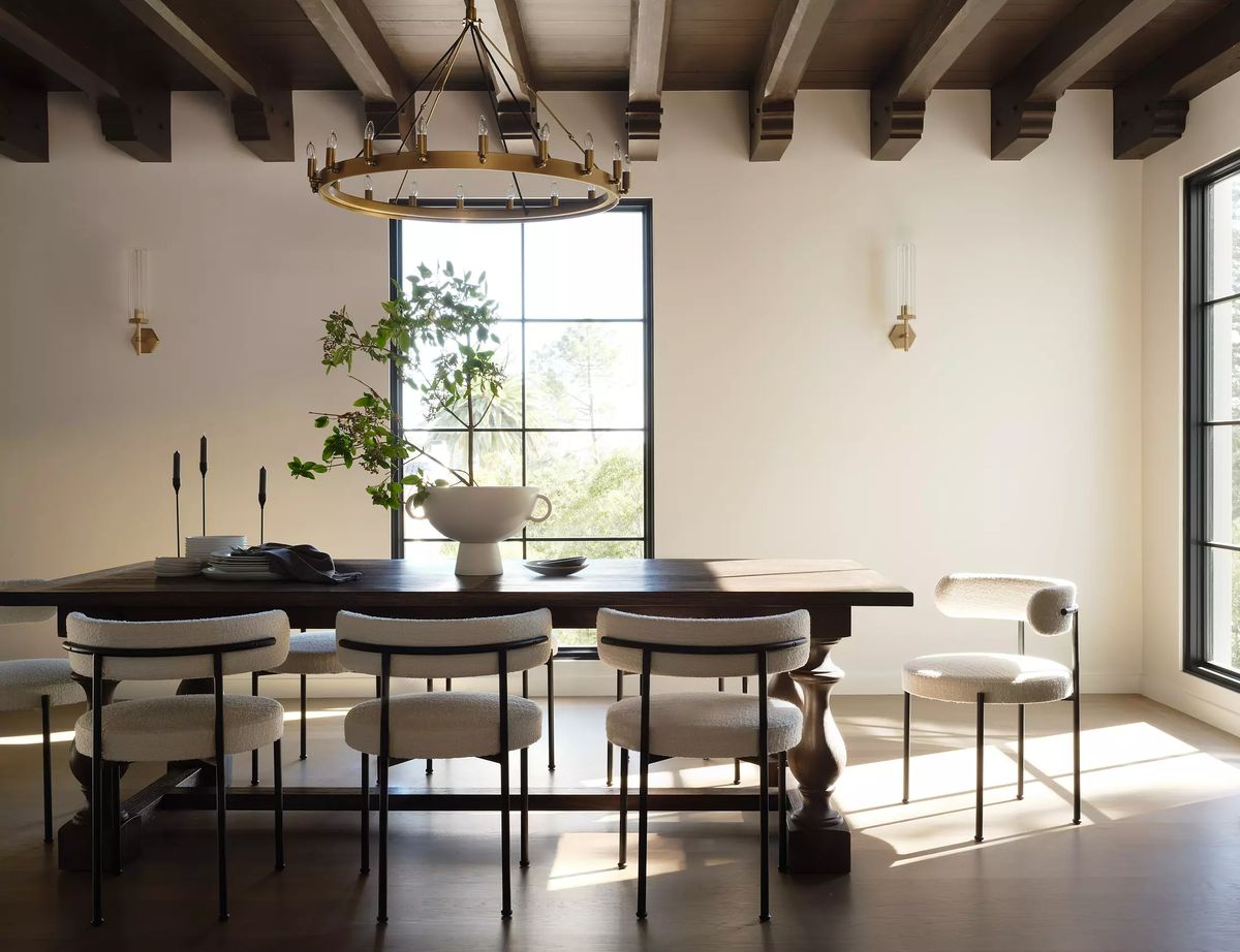Dining room with large table, eight chairs, serving bowl, plant, windows, and exposed beam ceiling.